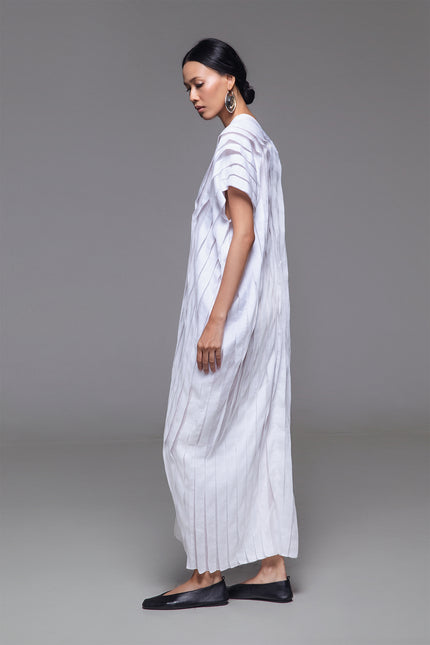 Model wearing Naria Kaftan in light cotton with floor-length straight silhouette, full vertical pleats, and V-neckline for a clean, architectural look.