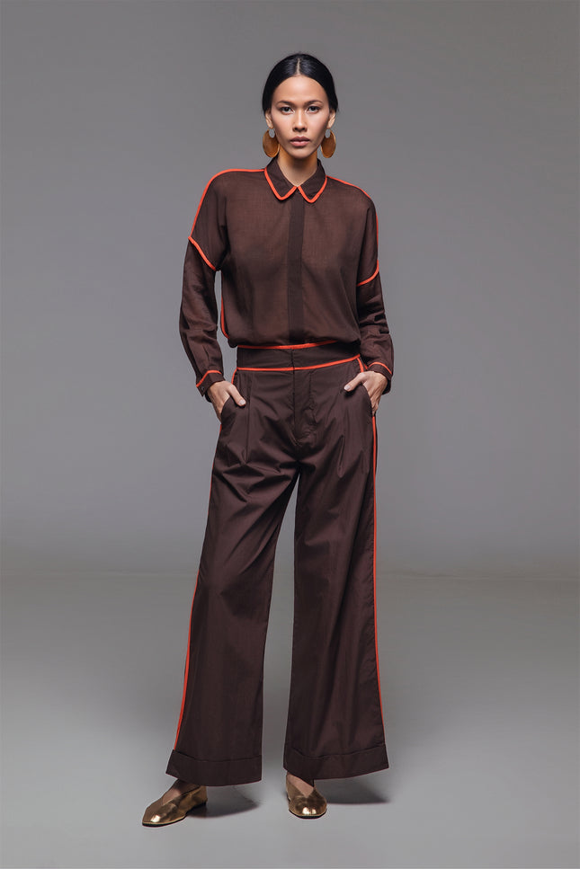 Model wearing Neal Pants in lightweight cotton, featuring a high waist, full-length silhouette, front pleats, cuffed hem, and contrast piping detail.