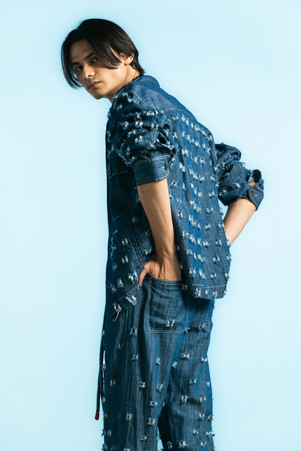Model wearing the Olwen Jacket in 100% cotton, featuring a boxy silhouette, button-front closure, four pockets, and raw, textured denim with uneven threads.