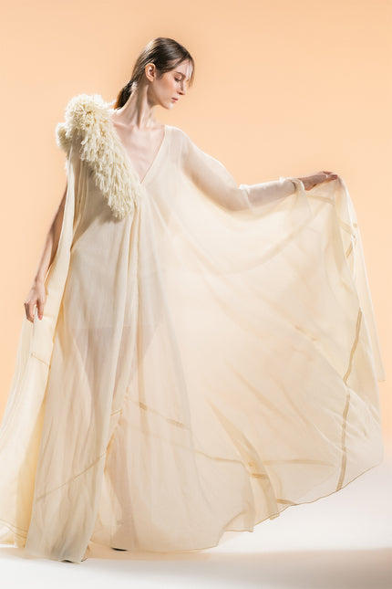 Model wearing Nehara Dress in an ethereal flowing silhouette, featuring a V-neckline and three-dimentional hand-cut fringe detailing on the shoulder in a soft bone tone.
