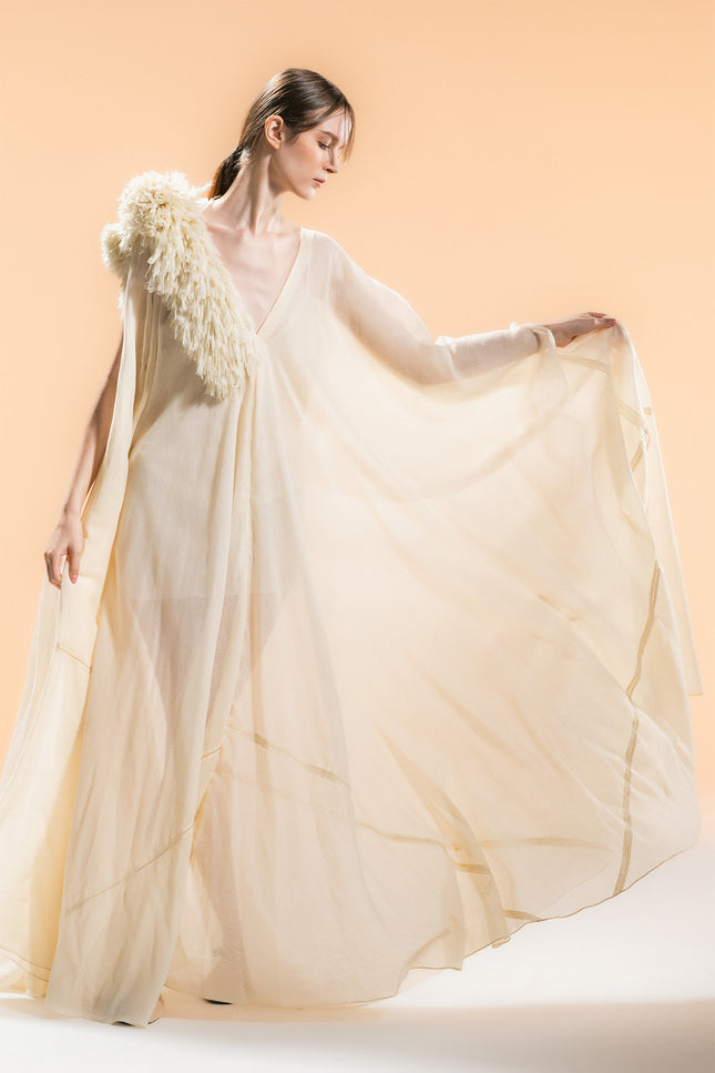 Model wearing Nehara Dress in an ethereal flowing silhouette, featuring a V-neckline and three-dimentional hand-cut fringe detailing on the shoulder in a soft bone tone.