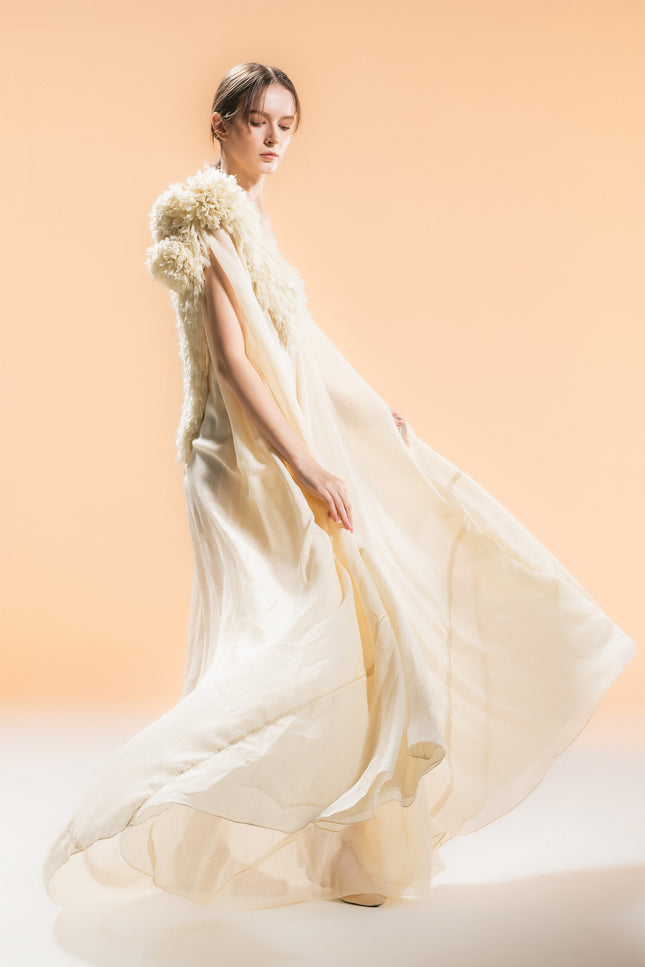 Model wearing Nehara Dress in an ethereal flowing silhouette, featuring a V-neckline and three-dimentional hand-cut fringe detailing on the shoulder in a soft bone tone.