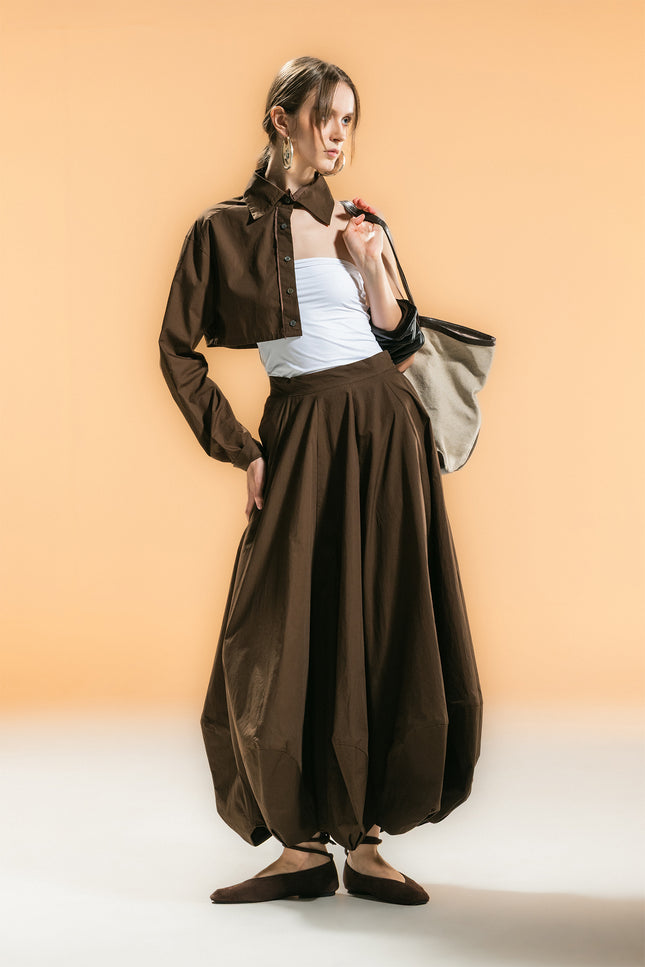 Model wearing Orla Half Shirt with a cropped one-sided silhouette, single long sleeve, cropped fit, button-down front, and detachable waist strap.