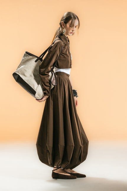 Model wearing Orla Half Shirt with a cropped one-sided silhouette, single long sleeve, cropped fit, button-down front, and detachable waist strap.