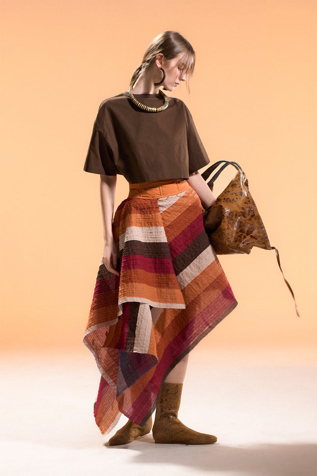 Model wearing the Orphia Skirt with an adjustable wrap design, asymmetrical pointed hem, and multicolored diagonal appliqué stripes on a nylon base.