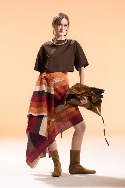 Model wearing the Orphia Skirt with an adjustable wrap design, asymmetrical pointed hem, and multicolored diagonal appliqué stripes on a nylon base.