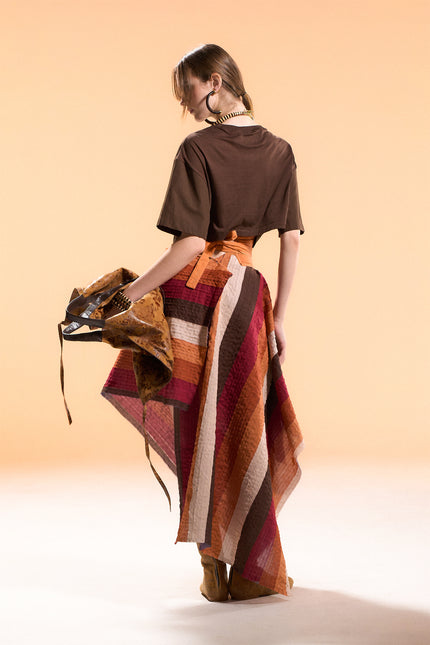 Model wearing the Orphia Skirt with an adjustable wrap design, asymmetrical pointed hem, and multicolored diagonal appliqué stripes on a nylon base.
