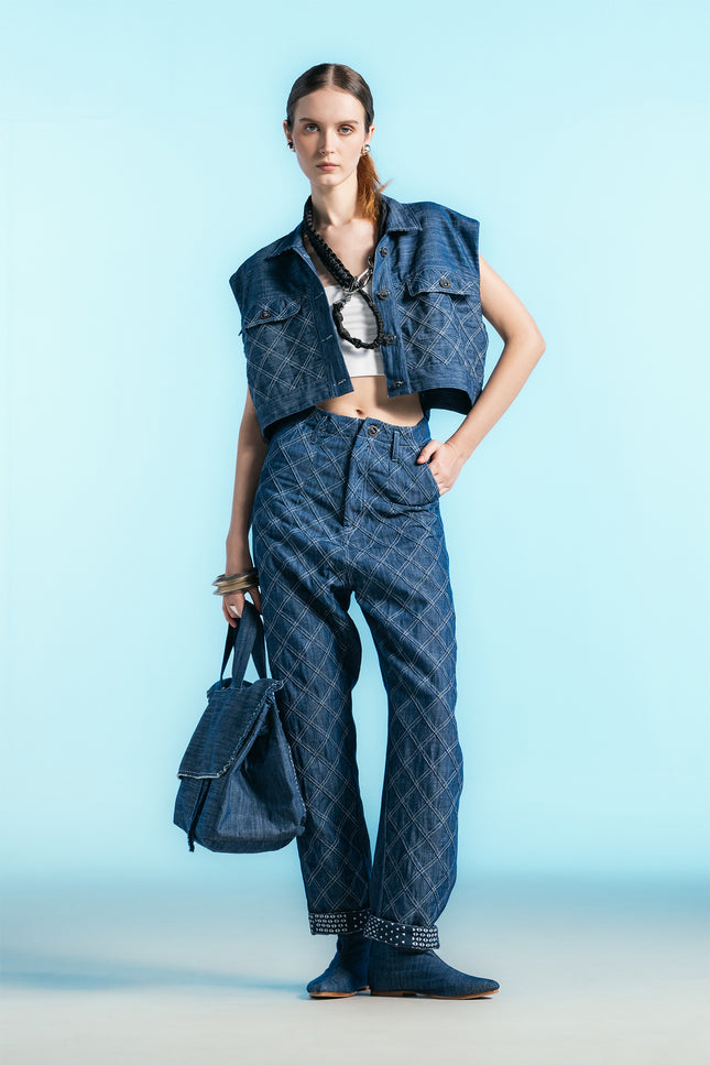 Model wearing Nena Jacket in cotton denim, featuring a cropped sleeveless silhouette and diamond-patch textured detailing.