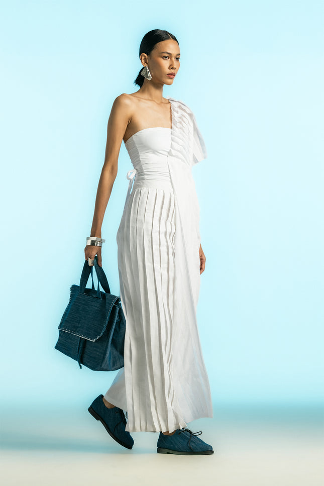 Model wearing Nyma Dress in lightweight cotton, featuring a sculptural one-shoulder silhouette, layered pleats, asymmetrical design, and adjustable side tie.