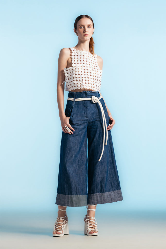 Model wearing white cropped top with coin-shaped appliqué texture and square neckline, paired with wide-leg trousers.