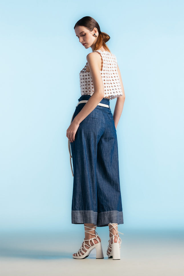 Model wearing white cropped top with coin-shaped appliqué texture and square neckline, paired with wide-leg trousers.