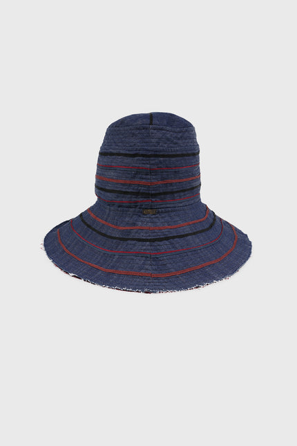 Model wearing Alvin Bucket Hat in indigo denim with multicolor ribbon detailing, structured silhouette, and contrasting lining.
