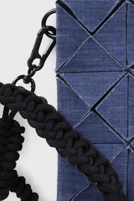 Model carrying the Oleander cotton clutch with an all-over geometric pleated texture and detachable knotted strap.