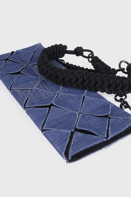 Model carrying the Oleander cotton clutch with an all-over geometric pleated texture and detachable knotted strap.