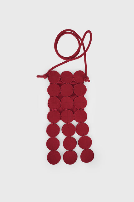 Model wearing a bold red Nysa Bag featuring coin applique detailing, an adjustable strap, and a magnetic snap closure, styled as a hands-free sling with playful dangling accents.