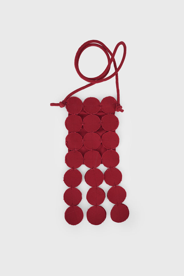 Model wearing a bold red Nysa Bag featuring coin applique detailing, an adjustable strap, and a magnetic snap closure, styled as a hands-free sling with playful dangling accents.